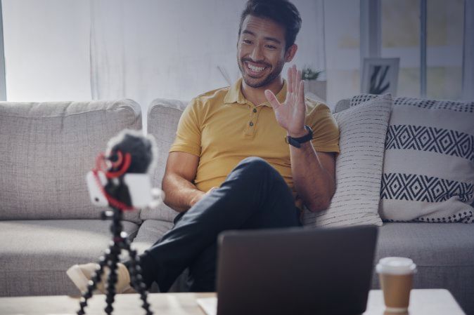 Hombre saludando a la webcam en su casa sentado en el sofá