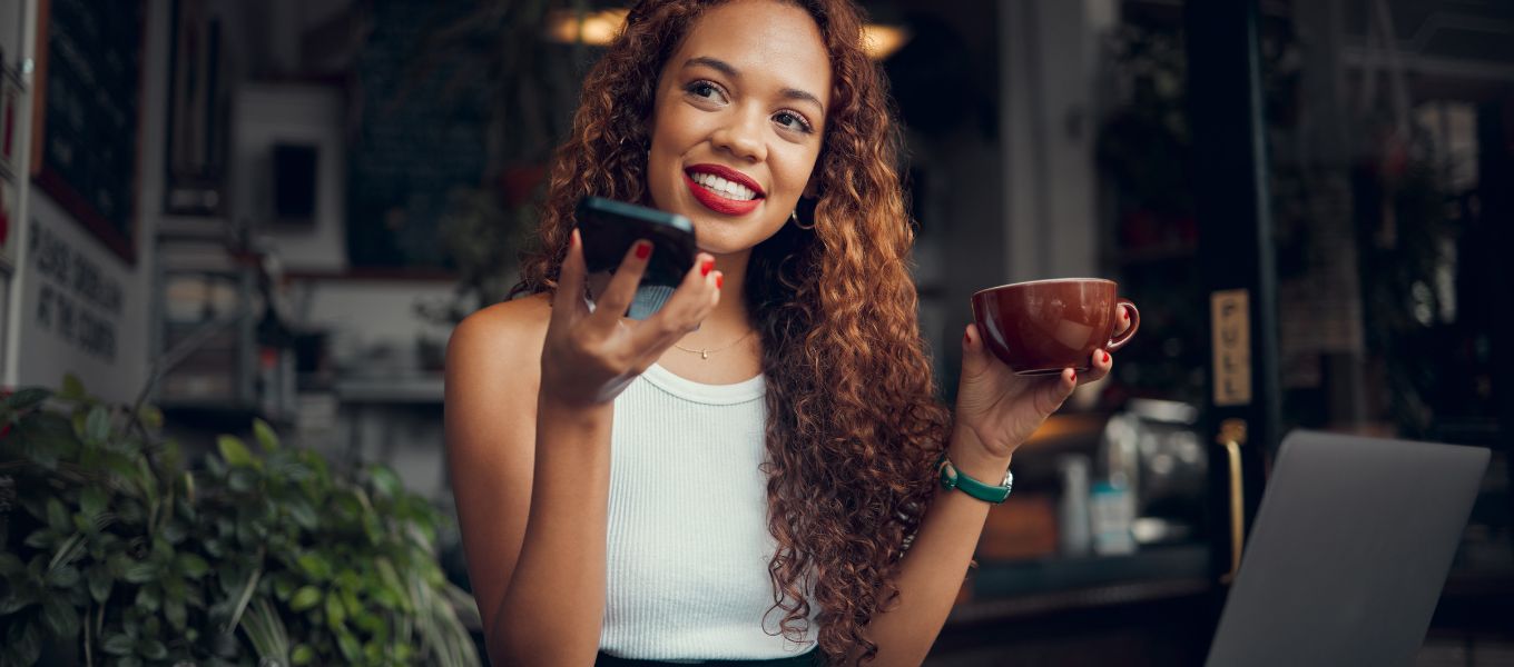 Bonita mujer usando el habla a texto en su teléfono en un café mientras bebe café